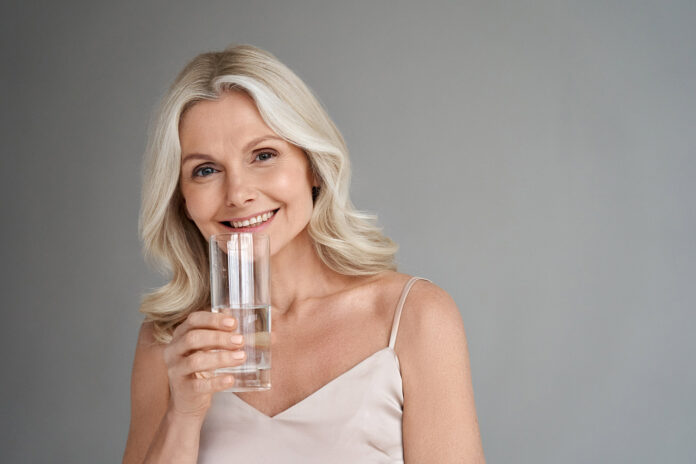 Smiling healthy thirsty fit mid aged 50s woman holding glass drinking water.