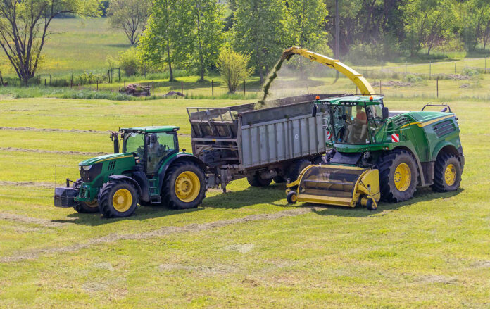 Self-Propelled forage harvester and tractor with silage trailer in the field
