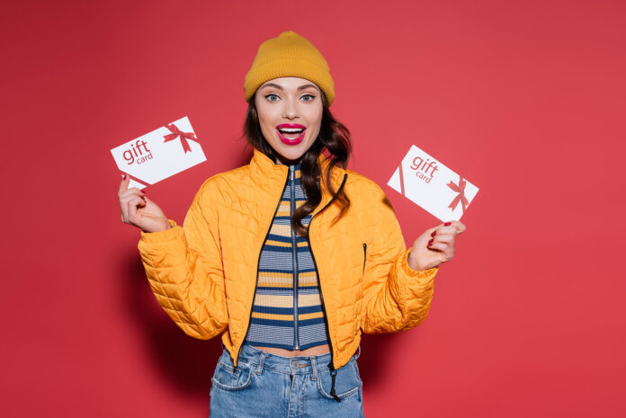 amazed young woman in beanie hat and orange puffer jacket holdin